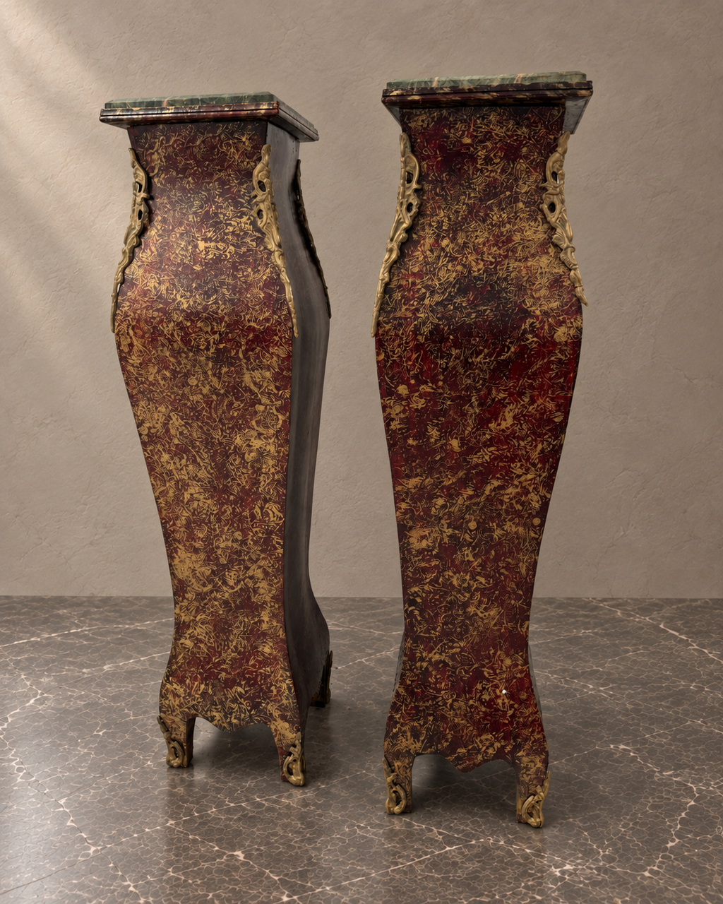 Pair of burgundy-and-gold decorative pedestals with green marble tops in a styled setting