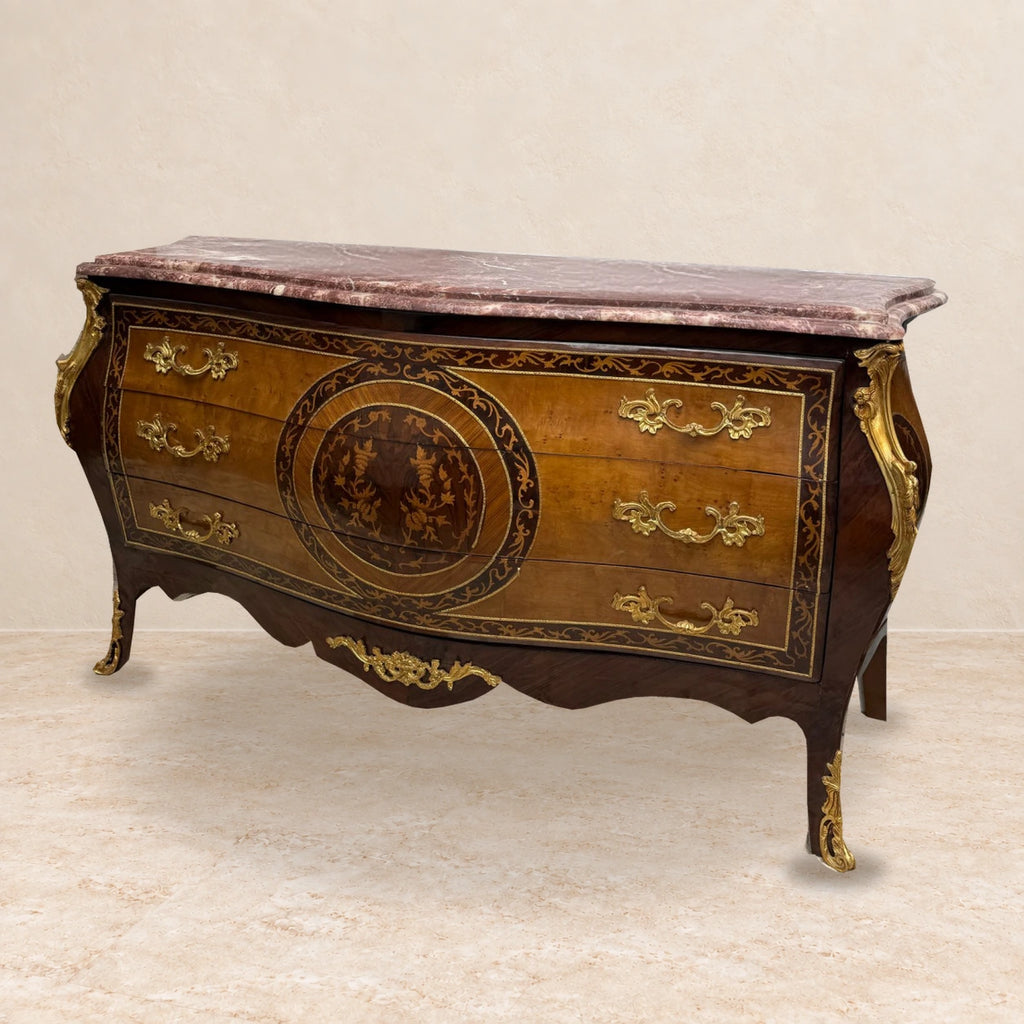 Louis XV-style chest with floral marquetry, bronze mounts and rose marble top, staged on a pale stone floor.