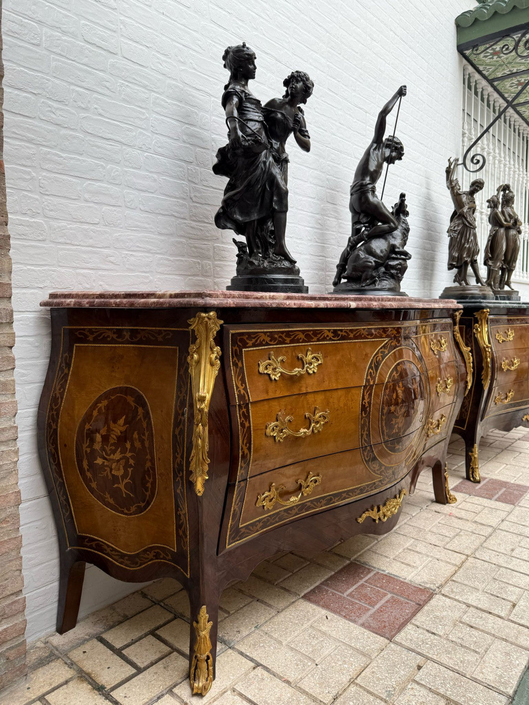 Original side view of the rose marble marquetry chest, showing its curved side panel and legs. Decorative objects are not included.